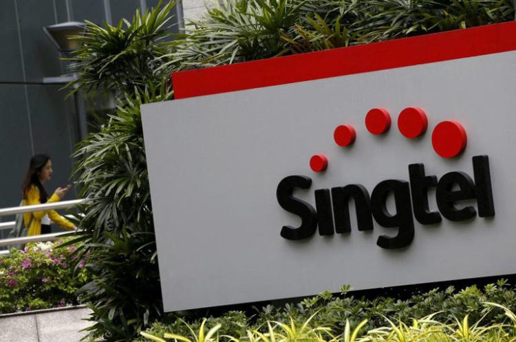 A woman using a mobile phone walks behind a Singtel signage at their head office in Singapore February 11, 2016. REUTERS/Edgar Su/File Photo