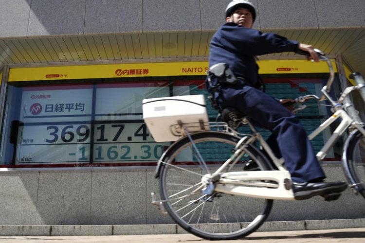 A police officer rides a bicycle past an electronic stock board showing Japan's Nikkei 225 index at a securities firm Friday, April 19, 2024, in Tokyo. Asian markets tumbled Friday, with Japan's benchmark Nikkei 225 down more than 3% on heavy selling of semiconductor-related shares
