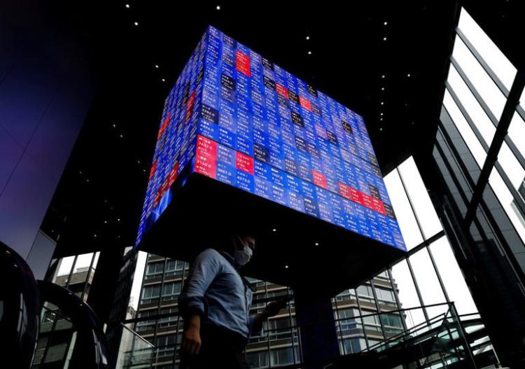A man walks under an electronic screen showing Japan's Nikkei share price index inside a conference hall in Tokyo, Japan June 14, 2022. REUTERS/Issei Kato/File Photo