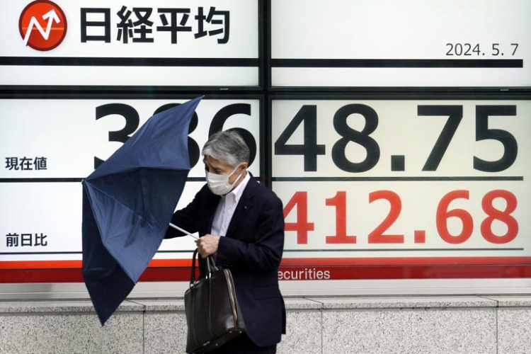 A person walks in the rain near an electronic stock board showing Japan's Nikkei 225 index at a securities firm Tuesday, May 7, 2024, in Tokyo.