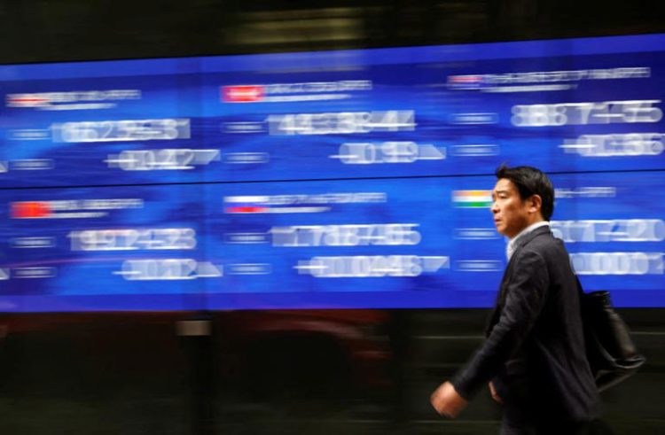 A passerby walks past an electric monitor displaying various countries' stock price index outside a bank in Tokyo, Japan, March 22, 2023.