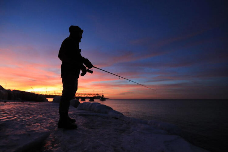 A man fishes on the frozen shoreline of Lake Erie as the sun sets in Cleveland, Ohio in 2022. NOAA issued a hazardous algae bloom for western Lake Erie on Thursday.