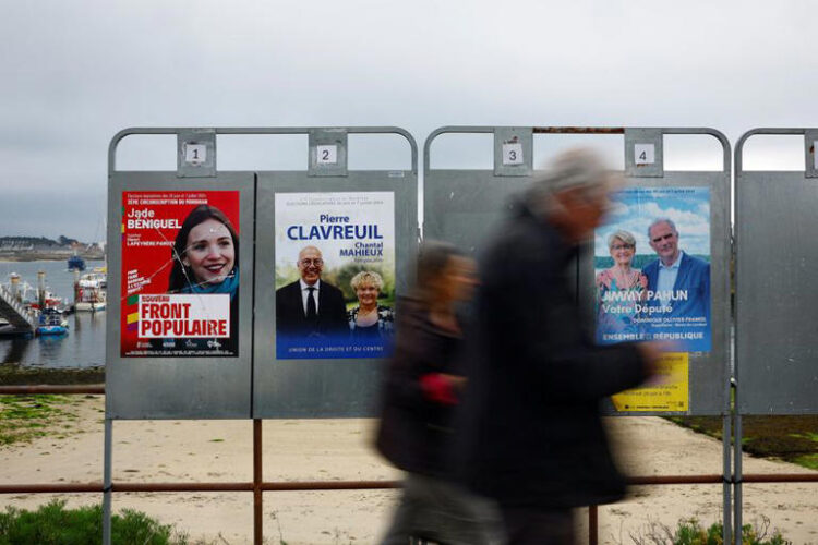 People walk past campaign posters on election boards ahead of the June 30 and July 7 French legislatives elections, in Quiberon, western France, June 20, 2024. REUTERS/Sarah Meyssonnier/File Photo