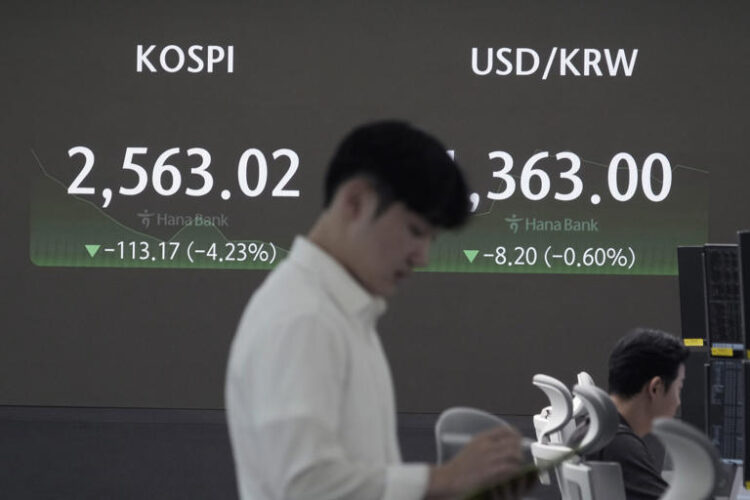 A currency trader works near a screen showing the Korea Composite Stock Price Index (KOSPI), left, and the foreign exchange rate between U.S. dollar and South Korean won at the foreign exchange dealing room of the KEB Hana Bank headquarters in Seoul, South Korea, Monday, Aug. 5, 2024.