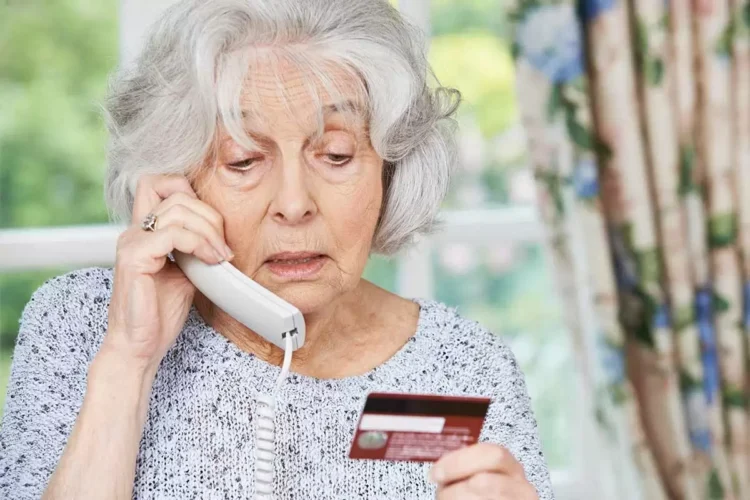 Concerned older woman looking at a credit card while on the phone.